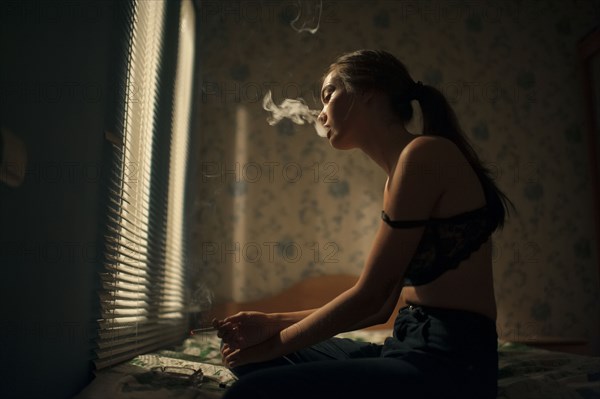Caucasian woman smoking in bedroom