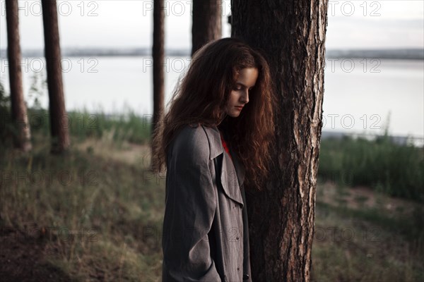 Caucasian woman standing behind tree near rural river