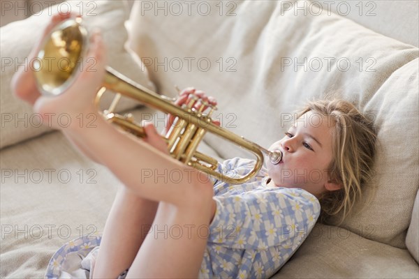 Caucasian girl on sofa playing trumpet