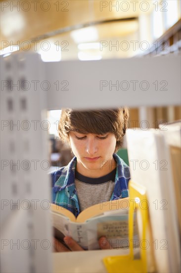 Mixed race boy reading book in library