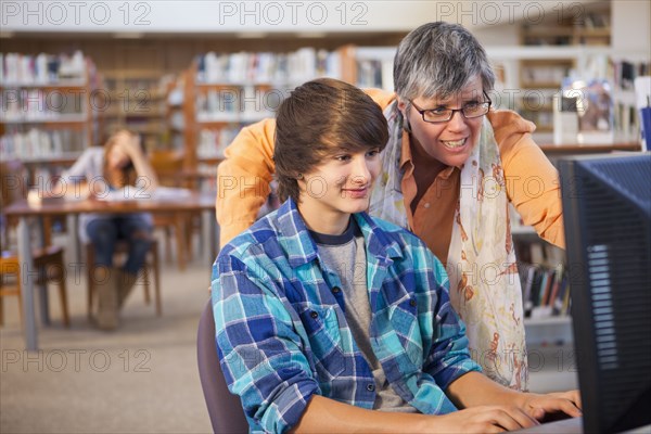 Librarian helping boy with computer in library