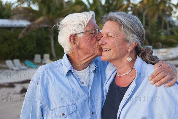 Caucasian man kissing wife on beach