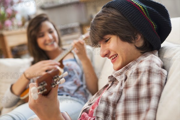 Mixed race friends playing ukuleles on sofa