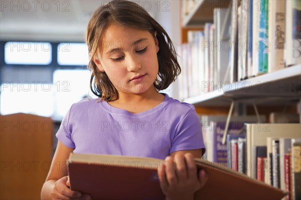 Mixed race girl reading book in library