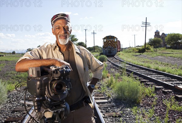 African American man with film camera near railroad tracks