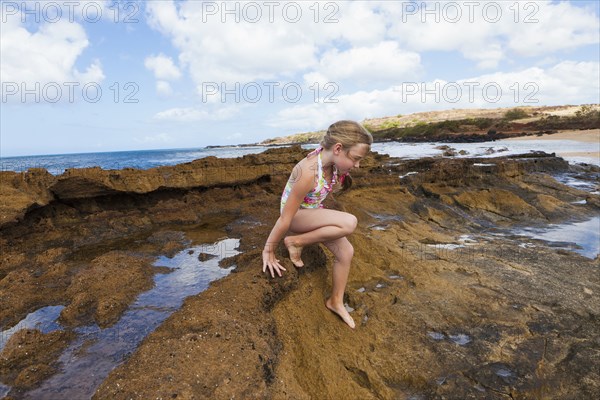 Caucasian girl playing on rocks near ocean