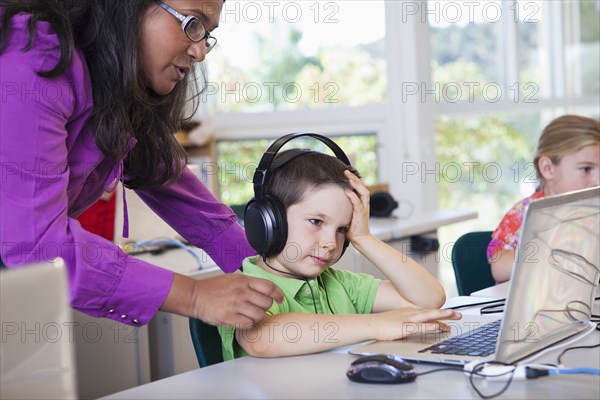 Teacher helping student using laptop in classroom