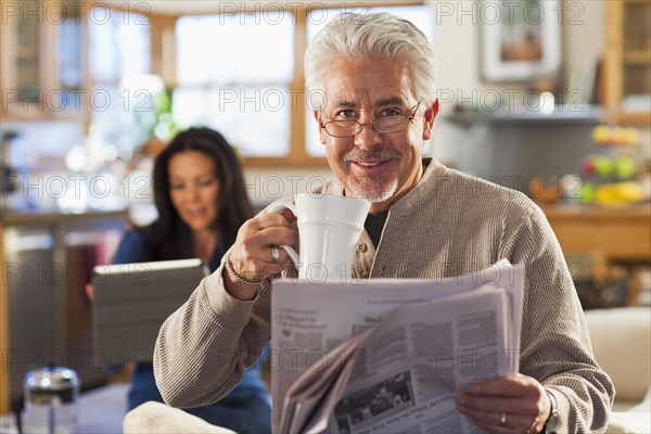 Hispanic man drinking coffee and reading newspaper