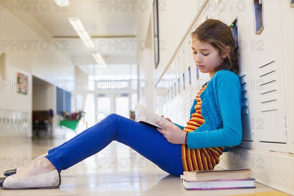 Caucasian student reading in school hallway