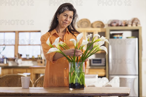 Older Hispanic woman arranging flowers in kitchen