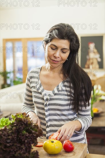 Older Hispanic woman chopping fruit in kitchen