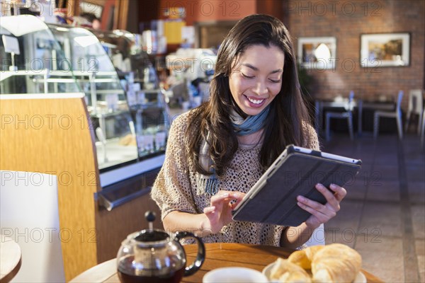 Mixed race woman using tablet computer in coffee shop