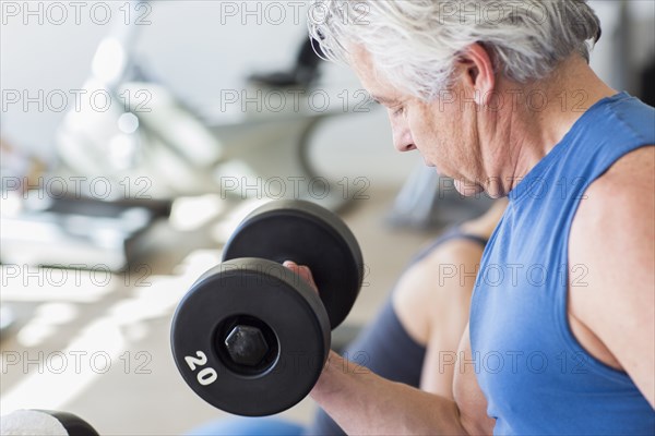 Older Hispanic man lifting weights in gym