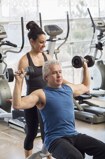 Older Hispanic man working with trainer in gym