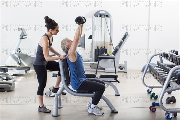 Older Hispanic man working with trainer in gym