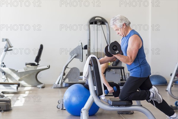 Older Hispanic man lifting weights in gym