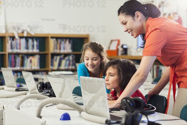 Teacher and children using laptop in library