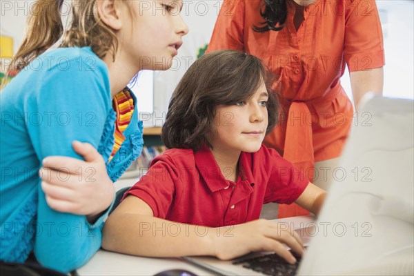 Teacher and children using laptop in library