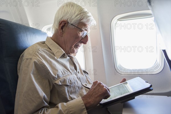 Older Caucasian man using tablet computer on airplane