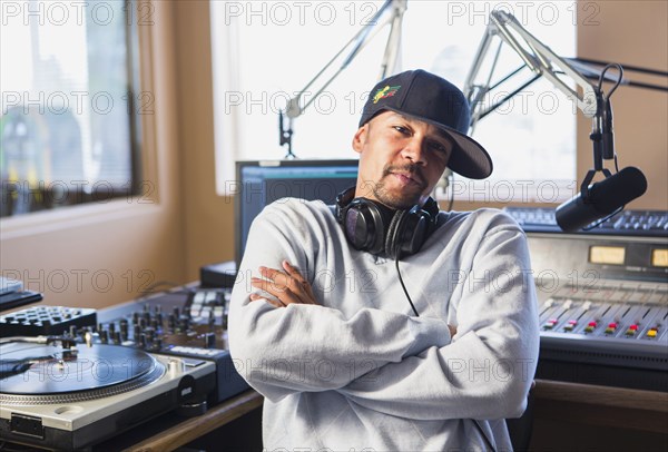 Mixed race disc jockey with arms crossed in studio