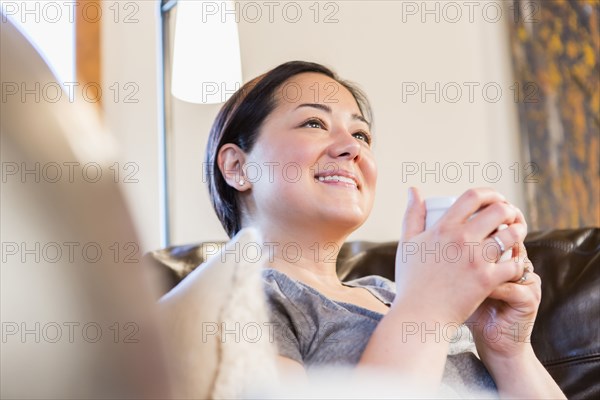 Mixed race woman having cup of coffee on sofa