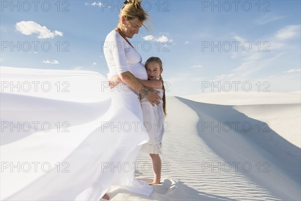 Pregnant Caucasian mother and daughter hugging in desert