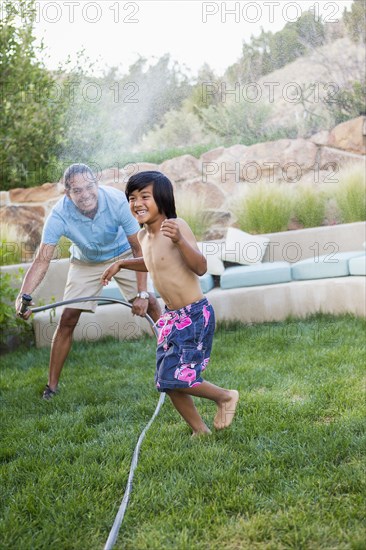 Father and son playing with hose in backyard