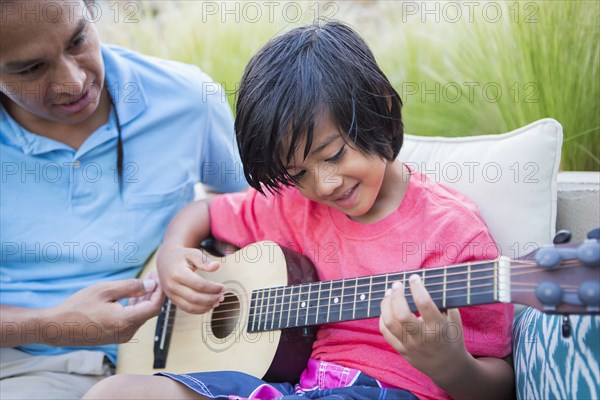 Father teaching son to play guitar outdoors