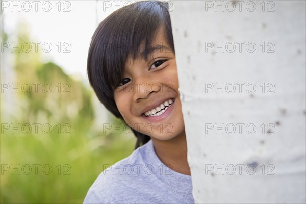 Boy peeking around tree outdoors