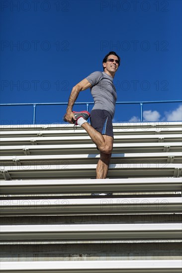 Hispanic athlete stretching on bleachers