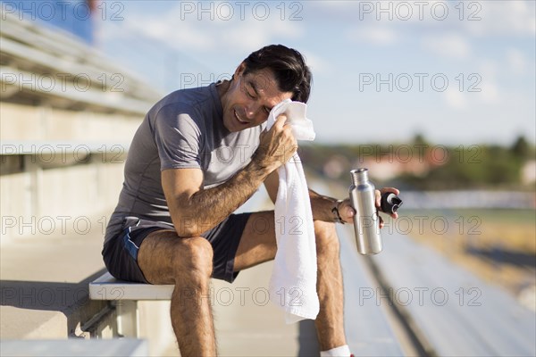 Hispanic athlete resting on bleachers