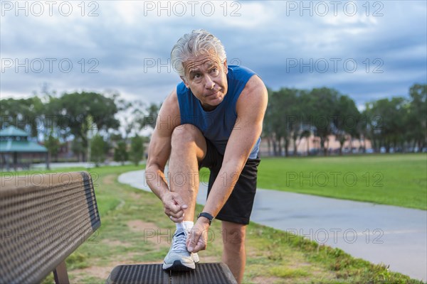 Hispanic man tying shoe in park