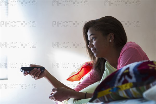 Mixed race teenage girl watching television on bed