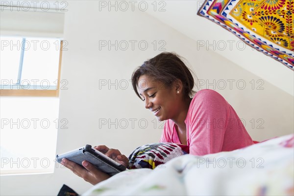 Mixed race teenage girl using digital tablet on bed