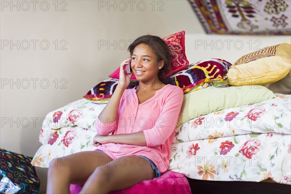 Mixed race teenage girl talking on cell phone in bedroom