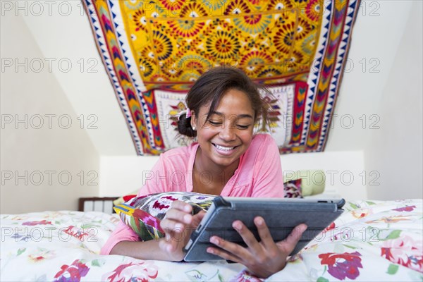 Mixed race teenage girl using digital tablet on bed