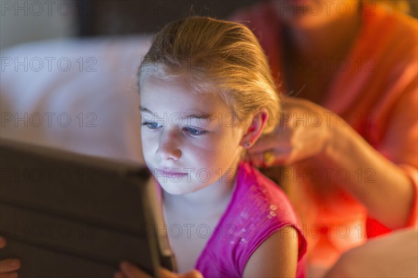 Caucasian girl using digital tablet as mother braids hair