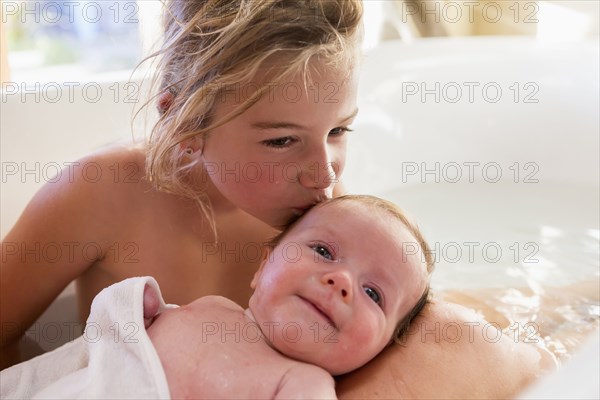 Caucasian girl kissing newborn baby in bath