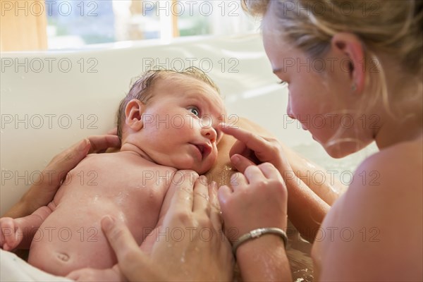 Caucasian girl washing newborn baby in bath