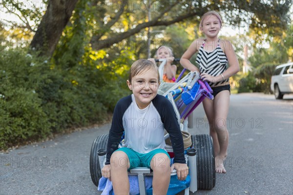 Children in swimsuits pushing cart on rural road