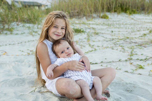 Girl cradling newborn boy on beach