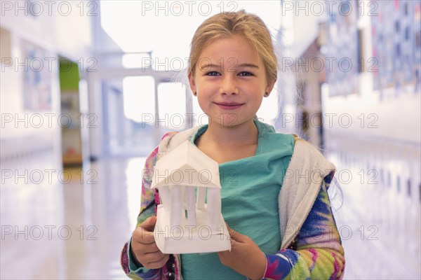 Caucasian girl holding art project in school corridor