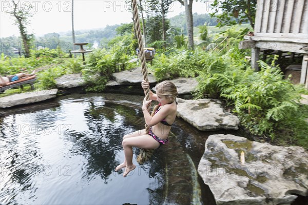 Caucasian girl swinging on rope above pool