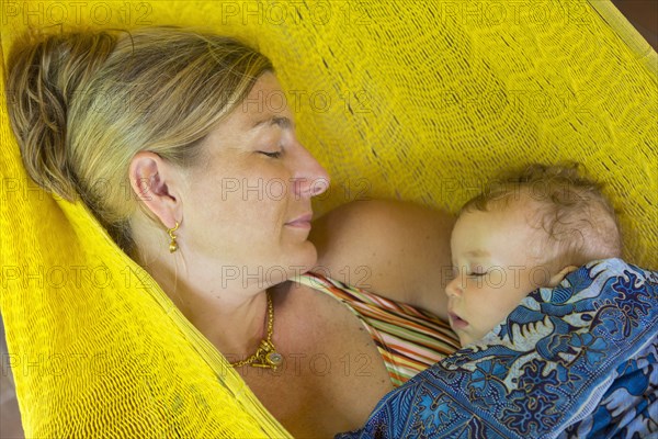 Caucasian mother and baby sleeping in hammock