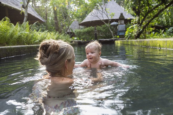 Caucasian mother and baby playing in pool