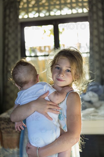 Caucasian girl carrying baby boy in bedroom