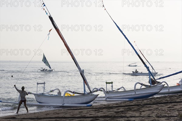 Fisherman pulling sailboat line on beach