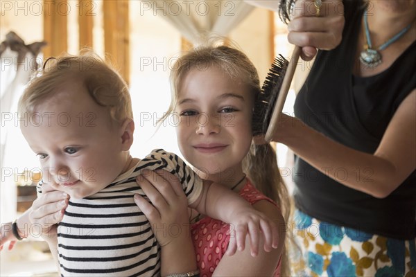 Caucasian girl holding brother as mother brushes her hair