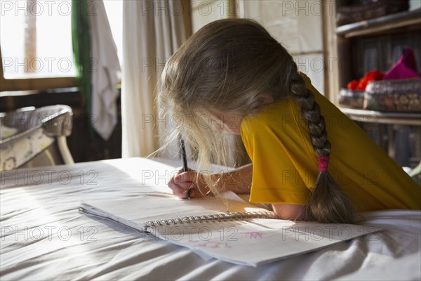 Caucasian girl drawing in notebook on bed