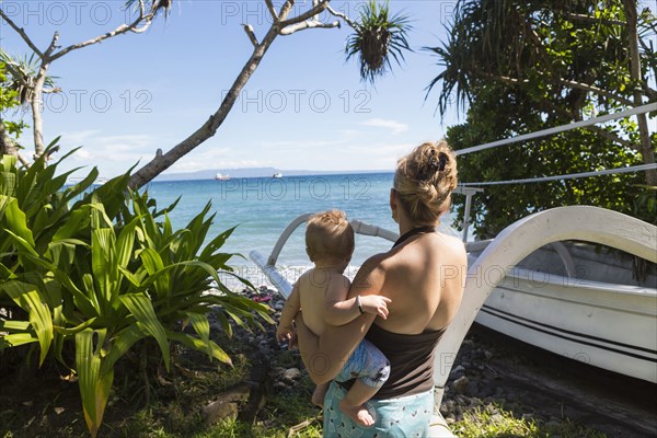 Caucasian mother carrying baby to tropical beach